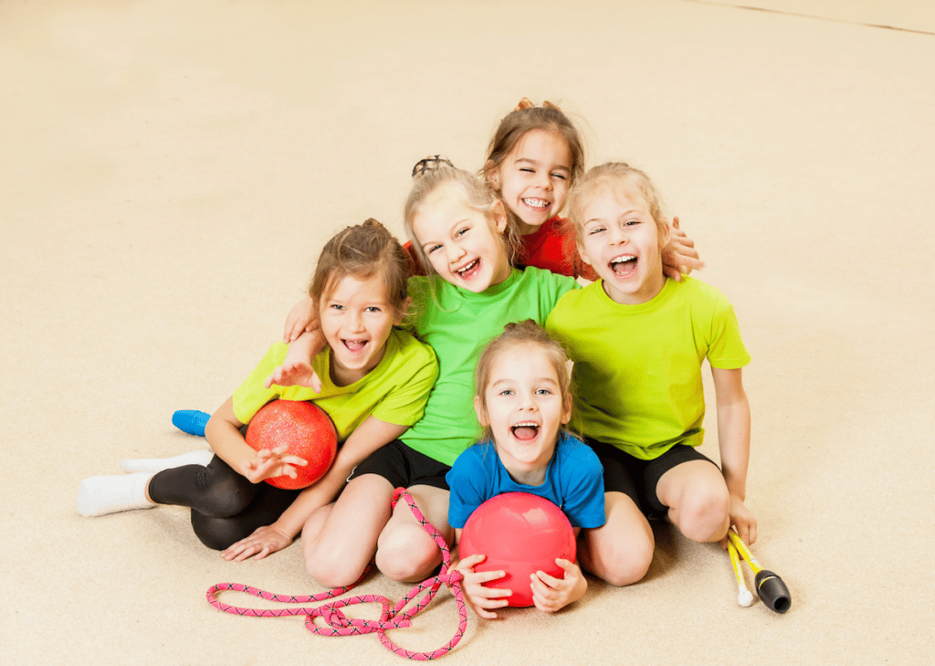 A group of kids sit together, smiling, holding gym equipment.