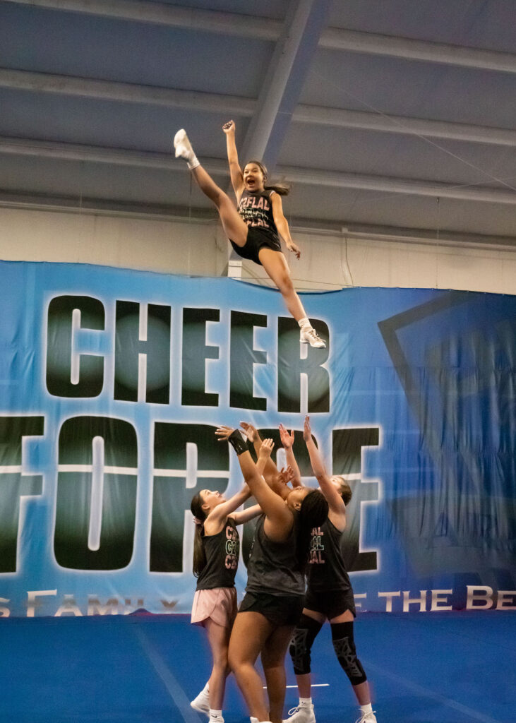 A group of cheerleaders throw one cheerleader in the air as part of a routine and wait to catch her.