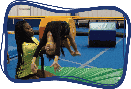 An instructor supports a student's back as she does a flip in the air.