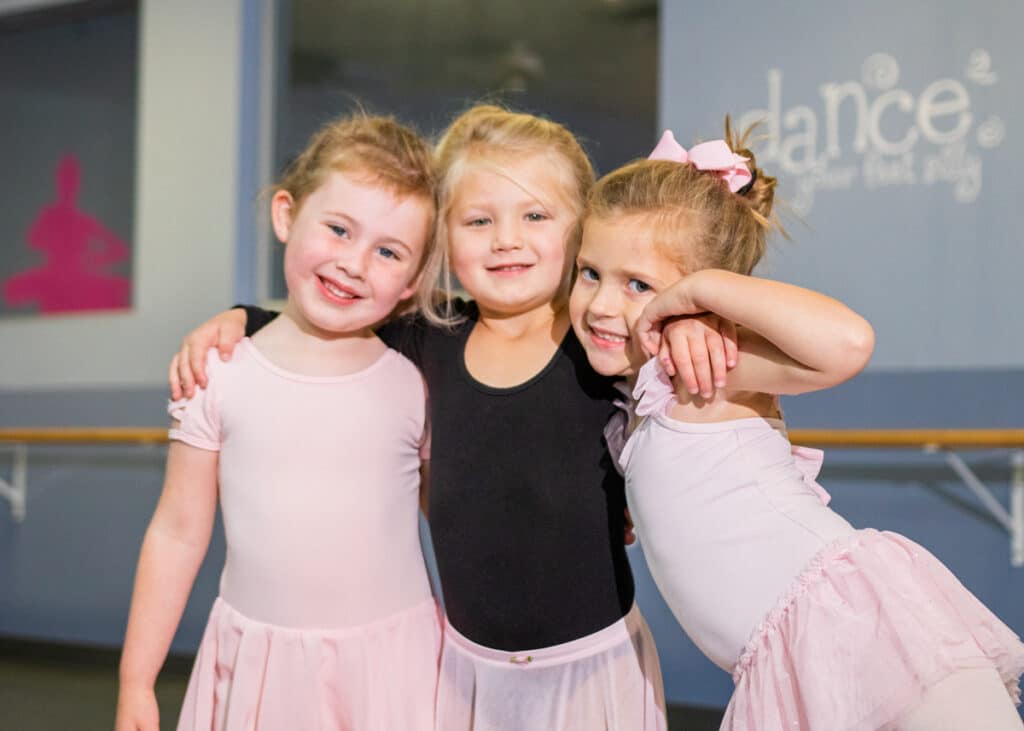 Three young girls hug and smile for the camera in their outfits for gymnastics.