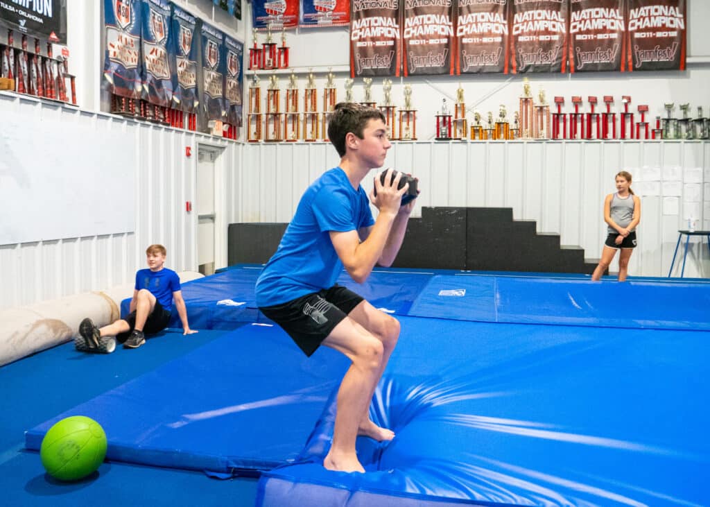A young boy prepares to jump into the air while on the training mats.