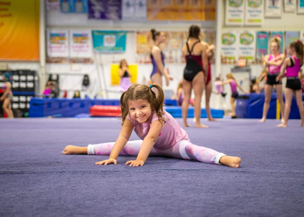 A little girl stretches on a mat before her class.